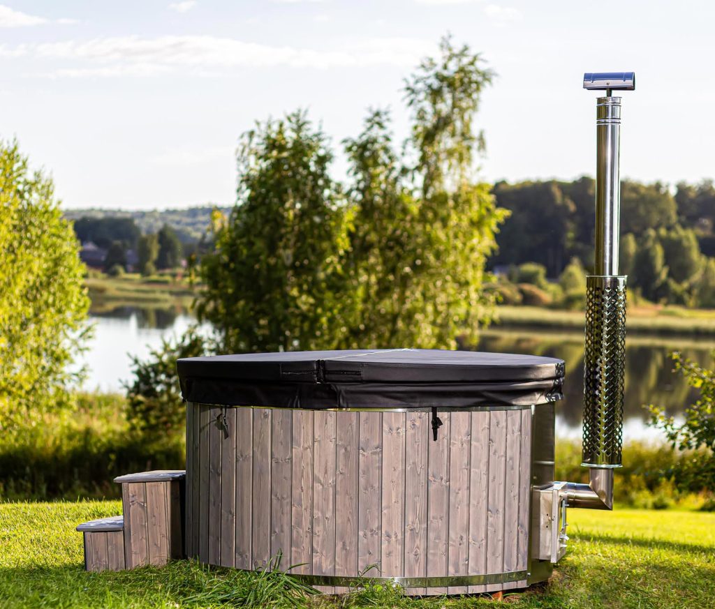 A wood stove hot tub sitting in the grass next to a lake